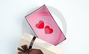 Two red hearts in an open gift box on a light background.