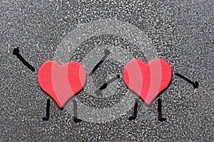 Two red hearts resembling a man with painted hands and feet on a gray background. Valentine`s Day. Funny hearts.