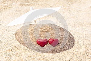 Two red hearts under beach umbrella on golden sand. St. Valentine Day and February 14th concept. Travel for love couple