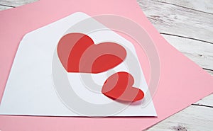 Two red hearts in a white envelope on a pink and wooden background, a copy of the space, the concept of Valentine's day