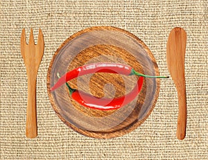 Two red hot chilli peppers on wooden plate over burlap