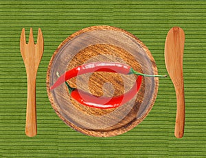 Two red hot chilli peppers on wooden plate over green cloth