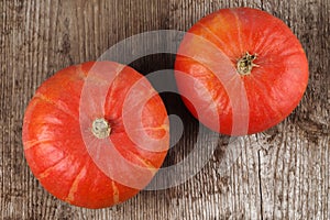 Two red kuri squashes on a rough woody texture background.