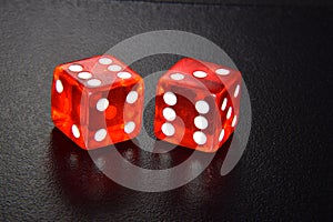 Two red luminescent casino dice on black reflecting background
