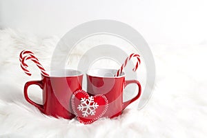 Two red mugs with candy cane on white fur background