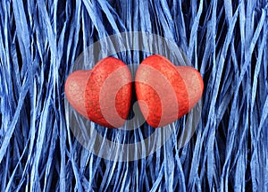 Two red painted polyfoam hearts on blue paper raffia background. Closeup.