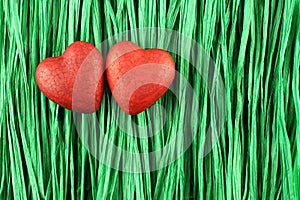 Two red painted wooden hearts on green paper raffia strips background