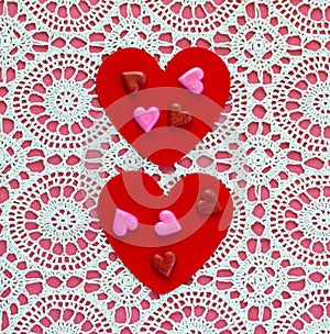 Two red hearts with heart shaped candies on a white doily against a pink background