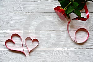 Two red paper hearts and tree red roses on a white wooden background.