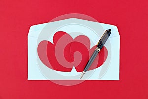 two red paper hearts on white envelope and black business pen