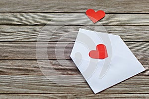 Two red paper hearts on white open envelope against gray wooden background