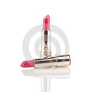 Two red and pink lipsticks in golden tube on white background with mirror reflection on glass surface isolated closeup, open lipst