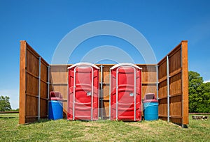 Two red portable restrooms in a park