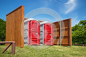 Two red portable restrooms in a park