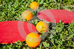 Two red rackets and four orange table tennis balls lie on the green grass. Close-up