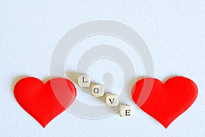 Two red silk hearts and the inscription love on a white sparkling background. Concept for Valentine`s day greeting card