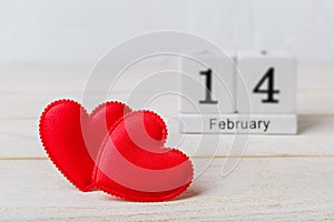 Two red silk valentine hearts and wooden perpetual calendar with date 14 february on a white wooden textured background. Concept