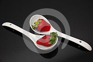two red strawberries on white spoon and black background