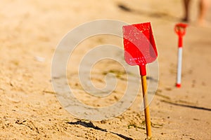 Two red toy shovels in sand on beach