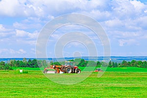 Two red tractors with a large mower in a field under a blue sky mow the grass. Haymaking, silage harvesting.