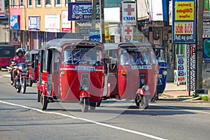 Two red tuk-tuks driving along a city street, Sri Lanka. Ambalangoda