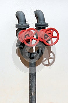Two red valves on black pipes against white wall background on a sunny day