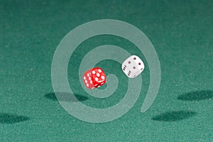 Two red and white dices falling on a green table