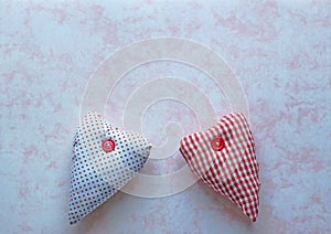 Two red and white fabric hearts on a pink marbled paper background