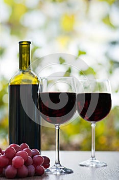 Two red wine glass and bottle on rustic wood surface