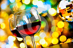 Two red wine glasses against colorful bokeh lights and sparkling disco ball background