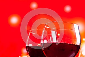 Two red wine glasses near the bottle against red lights background