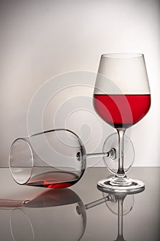 Two red wine glasses on a white background, one glass half full the second lies, spilled wine