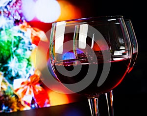 Two red wine glasses on wood table against christmas tree light background