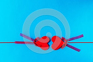 Two red wooden hearts on sticks with bows opposite each other on a blue background.