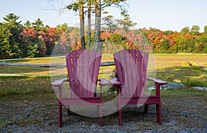 Two red wooden muskoka chairs in a park in autumn, fall season, Garden furniture. Sunny and warm fall season