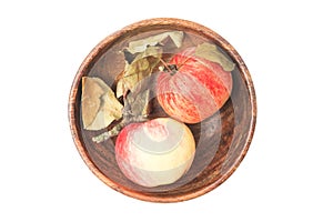 Two red and yellow-veined apples lie in round wooden bowl. Fruit has dry curled leaves. Autumn still life. harvest. Healthy food.