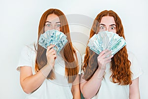Two redheaded young women both holding cash like playing cards standing on isolated white backgroung, money earning concept