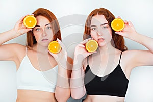 Two redheaded young women both standing on isolated white backgroung holding one half of orange near head and another near chin ,