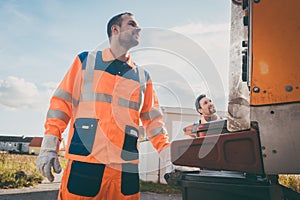 Two refuse collection workers loading garbage into waste truck