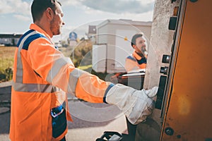 Two refuse collection workers loading garbage into waste truck