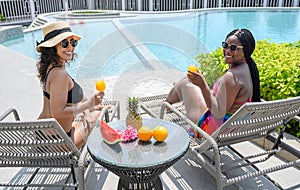 Two relax woman in swimwear sitting on sun bed with orange juice in summer time. holiday vacation concept