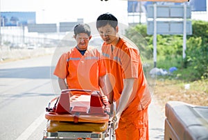 Two rescue staff in orange uniform putting a stretcher into an ambulance