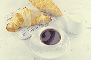 Two Ð°resh  croissants on a wooden vintage board in provence style with a cup of hot black coffee out of focus