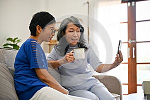 Two retired middle-aged Asian women enjoying talking with their grandchild through a video call