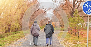 Two retired women dressed in jackets are engaged in Nordic walking in an autumn park in the middle of the trees. Rear