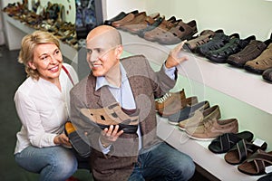 Two retirees together choosing pair of shoes for men in shoe store