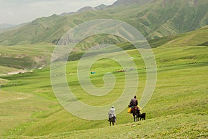 Two riders on horseback go away in the valley between the green mountains