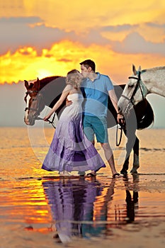 Two riders on horseback at sunset on the beach. Lovers ride horseback. Young beautiful man and woman with a horse at the sea. Rom