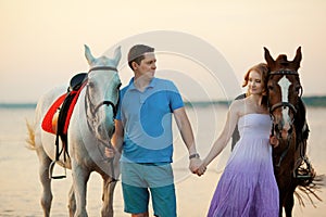 Two riders on horseback at sunset on the beach. Lovers ride horseback. Young beautiful man and woman with a horse at the sea. Rom