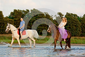 Two riders on horseback at sunset on the beach. Lovers ride horseback. Young beautiful man and woman with a horses at the sea.